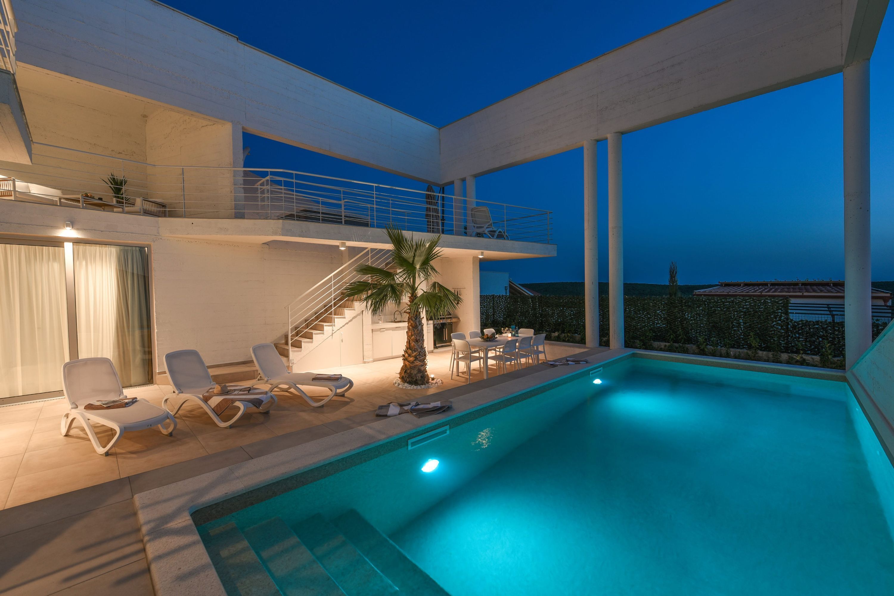 A modern poolside area with lounge chairs, a staircase, and a view of the sea.