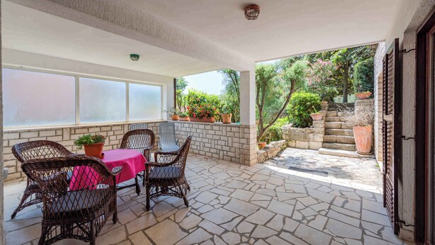 A covered patio with stone flooring, wicker furniture, and potted plants. - Holiday apartment with air conditioning (Valbandon)
