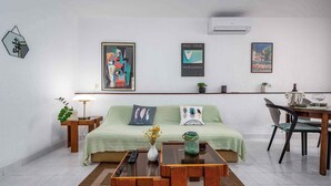 A modern living room with a green sofa, a coffee table, and a dining area with a chair and table. There are three framed artworks on the wall and a small plant on the shelf. - Holiday apartment with air conditioning (Valbandon)