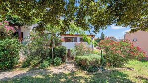 A residential garden with a pathway leading to a house with a red roof and white walls. - Holiday apartment with air conditioning (Valbandon)