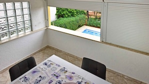 A room with a table, chairs, a window with blinds, and a view of a swimming pool. - Studio with air conditioning (Poreč)