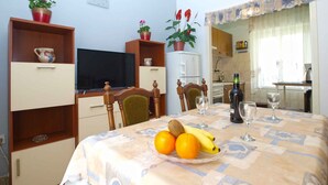 A dining area with a table set for two, a television, and a kitchen in the background. - Holiday apartment with terrace (Štinjan)