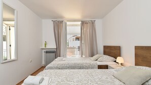 A hotel room with two beds, a nightstand with a lamp, a radiator, and a view of a building outside. - Holiday apartment with balcony and air conditioning (Rovinjsko Selo)