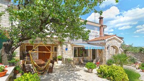 A stone house with a tiled roof, a hammock, outdoor seating, and potted plants. - Holiday apartment with balcony and air conditioning (Rovinjsko Selo)