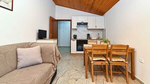 A compact living space with a sofa, a dining table with chairs, a kitchen area with white cabinets and a stove, and a television on a stand. - Holiday apartment with balcony and air conditioning (Rovinjsko Selo)