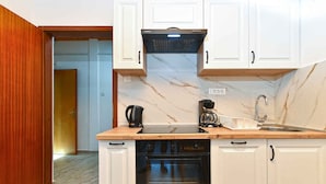 A kitchen with white cabinets, a black range hood, a built-in oven, a sink, and a countertop with a coffee maker and dish rack. - Holiday apartment with balcony and air conditioning (Rovinjsko Selo)