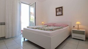 Un dormitorio con una cama, dos mesitas de noche, una ventana con cortinas, un radiador y un cuadro en la pared.
