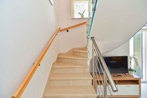 A staircase with a wooden handrail and beige steps leading to a room with a television and a plant.