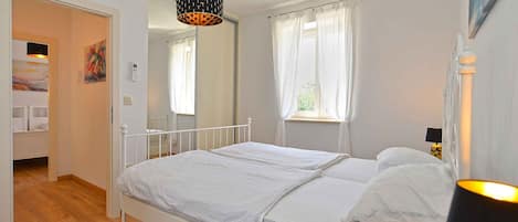 Une chambre avec un lit simple, une table de chevet, une lampe et une fenêtre avec des rideaux.