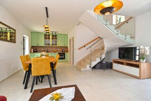 A modern living space with a dining area, kitchen, staircase, and a television. - Cottage with air conditioning (Matohanci)