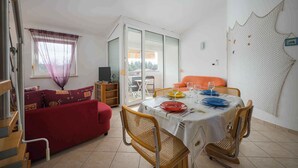 A dining area with a table set for four, a red sofa, and a sliding glass door leading to an outdoor balcony. - Holiday apartment mit Klimaanlage und Balkon (Monterol)