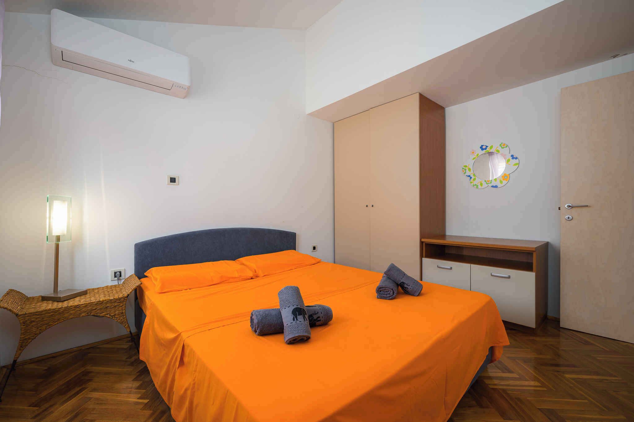 Una camera da letto con un letto, condizionatore d'aria, una scrivania, uno specchio e pavimento in legno.