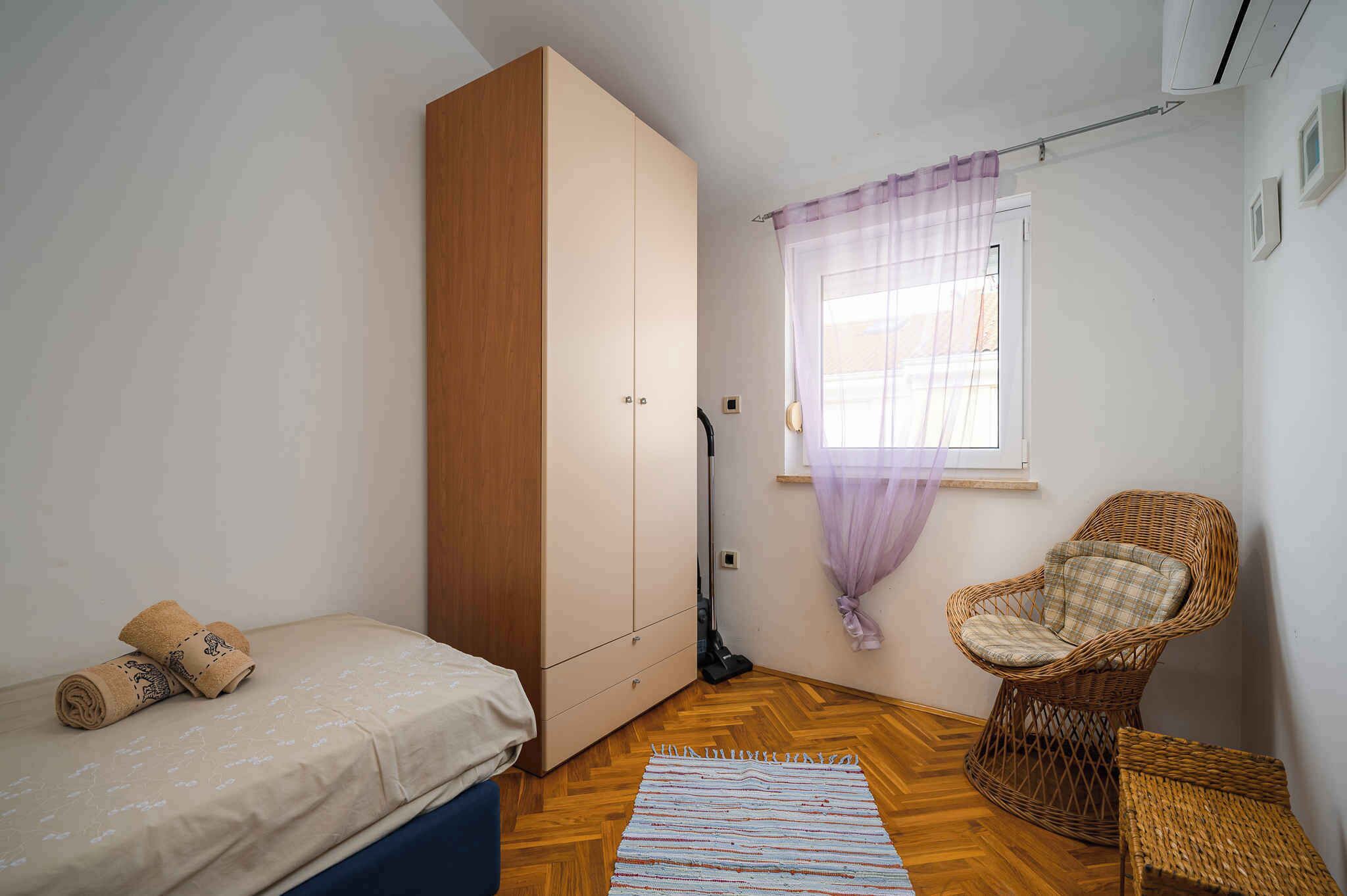Une chambre à coucher avec un lit, une armoire, une chaise et une fenêtre avec des rideaux.
