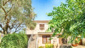 A two-story building with a staircase leading to the entrance, surrounded by greenery and trees. - Holiday apartment with air conditioning (Rovinj)