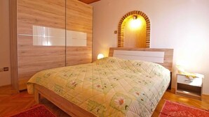 A bedroom with a wooden ceiling, a bed with a floral quilt, a red rug, a nightstand, and a wall-mounted light fixture. - Holiday apartment with air conditioning (Rovinj)