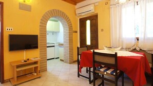 A dining area with a table set for two, a television on a stand, and a kitchen visible through an archway. - Holiday apartment with air conditioning (Rovinj)