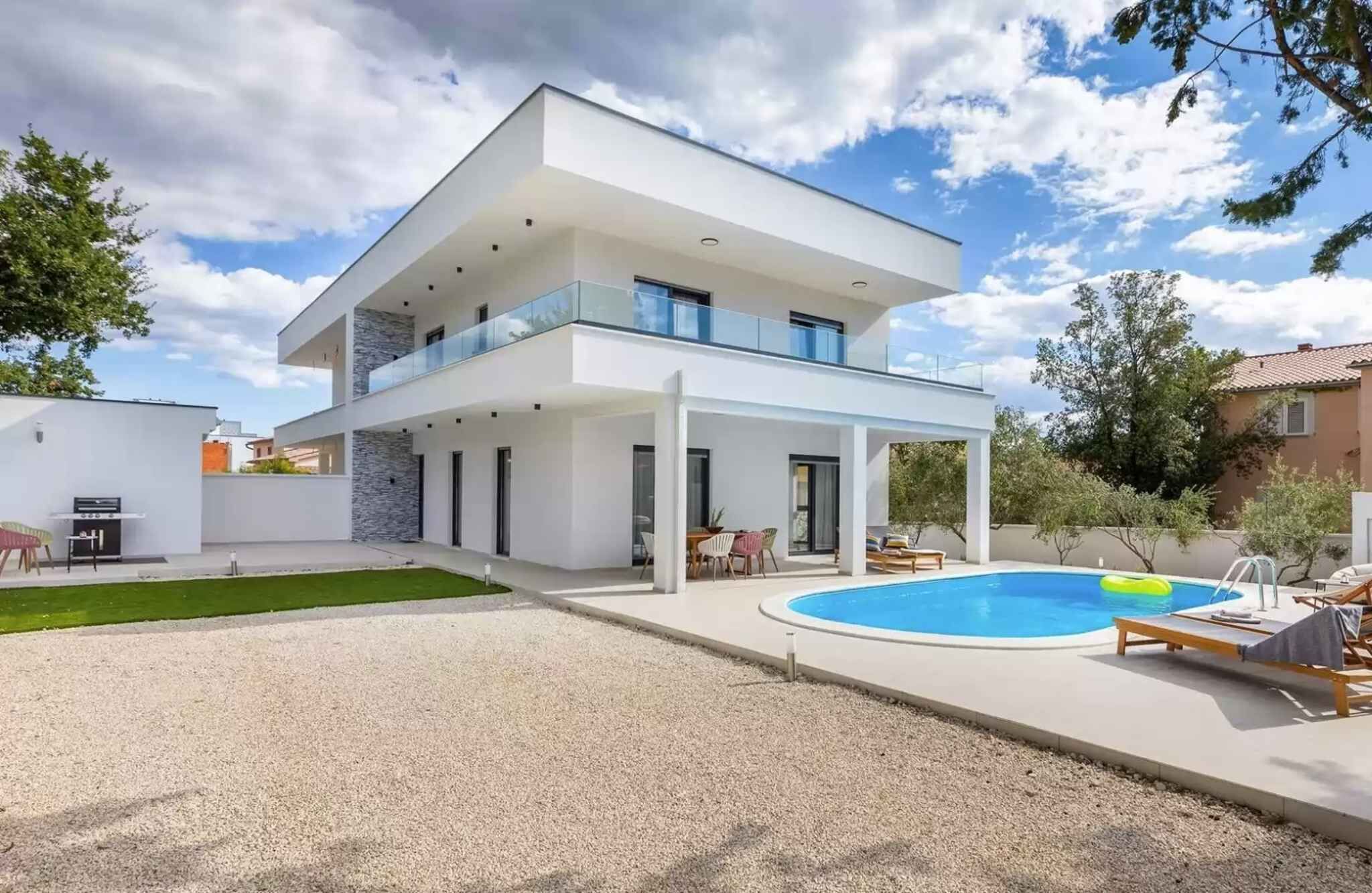 A modern two-story house with a covered patio, a swimming pool, and a well-maintained lawn.
