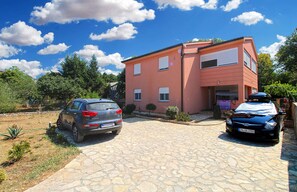 A two-story building with a paved driveway, parked cars, and surrounding greenery. - Holiday apartment with air conditioning (Valbandon)