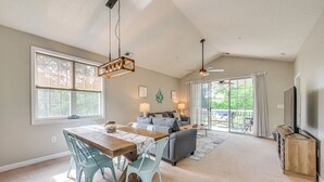 Un salon spacieux avec une table à manger en bois, des chaises bleu clair, un canapé gris et un ventilateur de plafond.