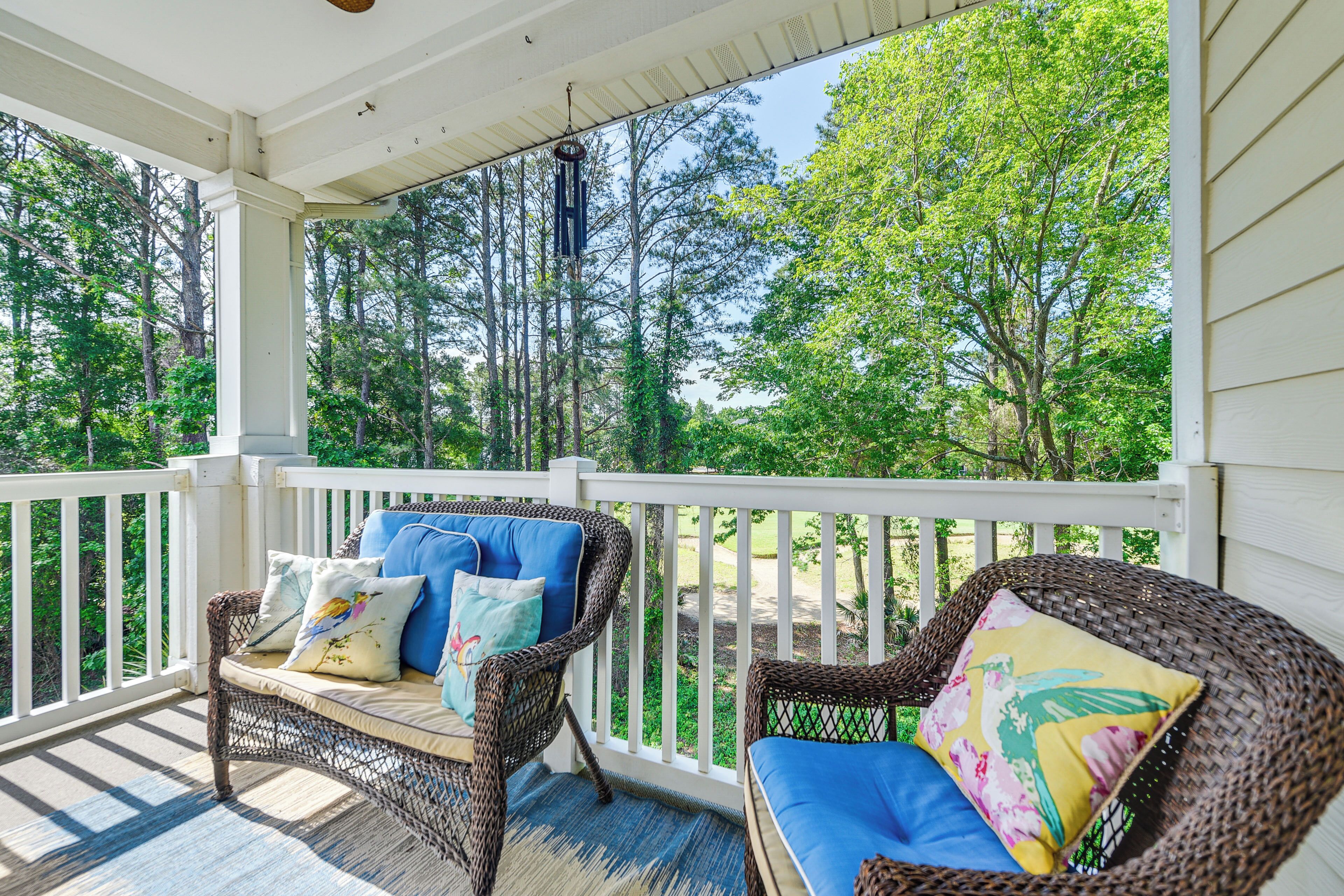 A covered porch with wicker furniture and white railings, overlooking a forested area.