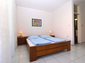 Une chambre à coucher avec un lit en bois, deux tables de chevet avec des lampes, un tableau encadré au mur et une porte donnant sur une autre pièce.
