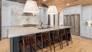 A modern kitchen with a large island, stainless steel appliances, and wooden bar stools. - Main Cabin - The Hendo (Henderson)