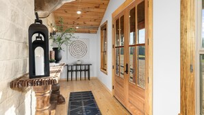 A hallway with wooden ceiling, a deer head mounted on the wall, a black lantern, a table with a plant, and large wooden doors. - Main Cabin - The Hendo (Henderson)