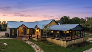 A log cabin with a stone pathway leading to the entrance, a covered deck, and a metal roof. - Main Cabin - The Hendo (Henderson)