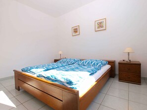 Quarto com cama de madeira, duas mesas de cabeceira e uma parede com duas fotos emolduradas.