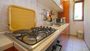 A compact kitchen with a gas stove, a microwave, and a small window. - Holiday apartment with air conditioning (Premantura)