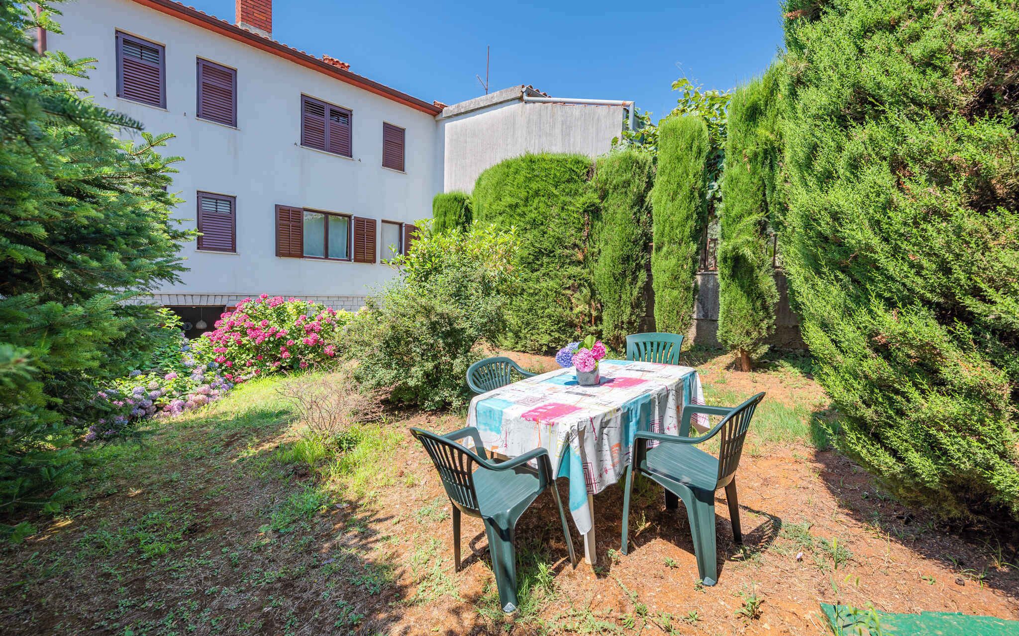 A patio with a table and chairs, surrounded by greenery and a building with windows.