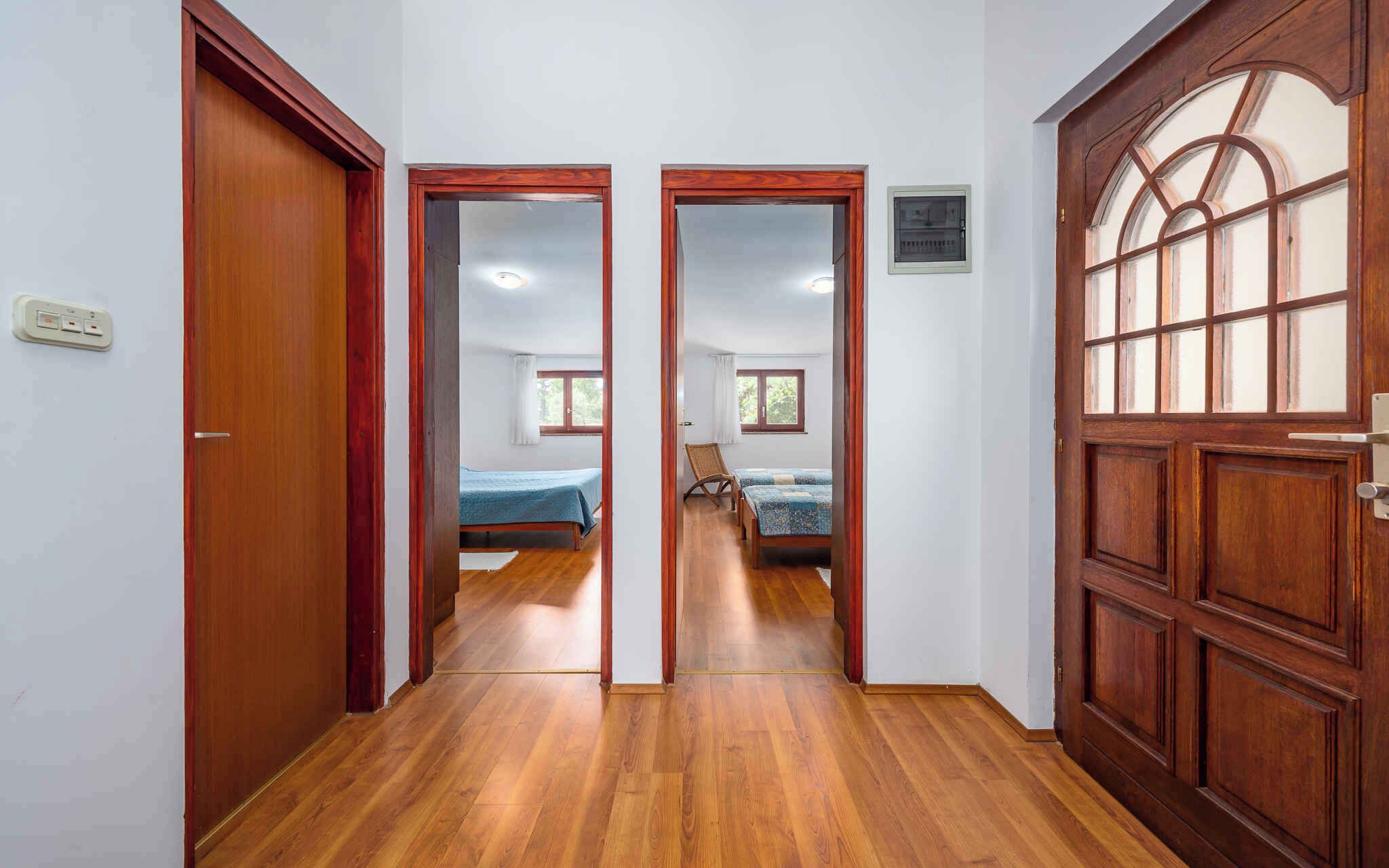 A hallway with wooden flooring leading to a bedroom with two beds and a window.