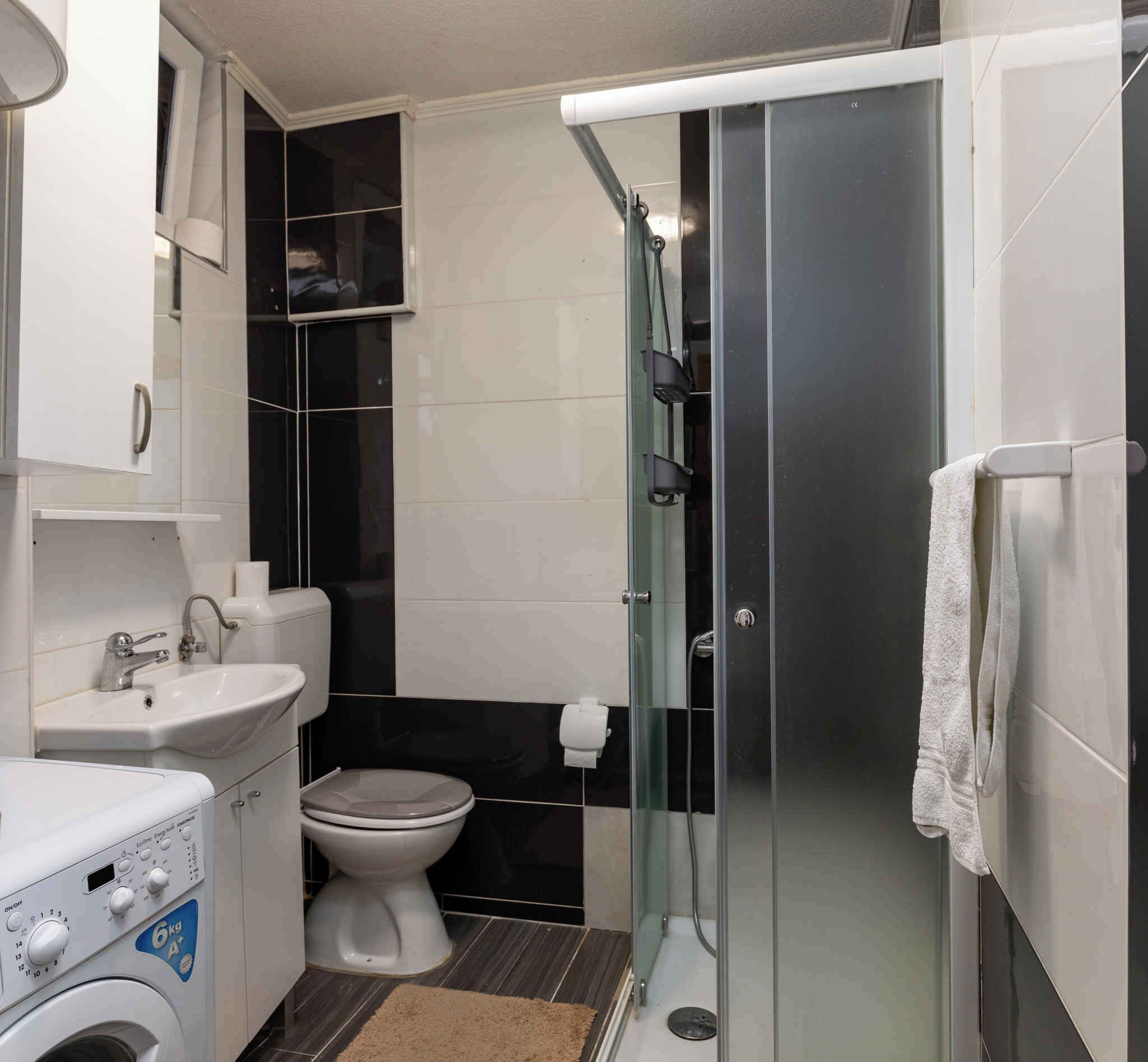 Une petite salle de bain équipée d’un lave-linge, de toilettes et d’une douche à parois en verre.