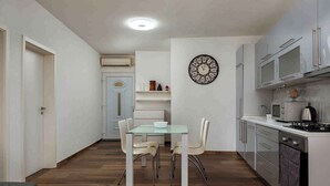 A compact kitchen with a dining area, featuring a glass table, white chairs, a wall clock, and modern appliances. - Holiday apartment with air conditioning (Pula)