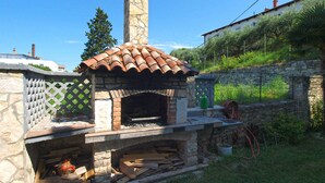 A stone-built outdoor pizza oven with a tiled roof, surrounded by a stone wall and a wooden fence. - Holiday apartment with air conditioning (Pula)