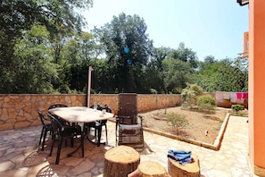 Um pátio externo com mesa e cadeiras de pedra, churrasqueira e parede de pedra.