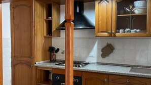 A kitchen with wooden cabinets, a gas stove, and a black range hood. - Mountain Relaxation  (Baunei)