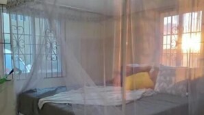 Een hemelbed met een baldakijn, een betegelde vloer en een raam met decoratieve ijzeren spijlen.