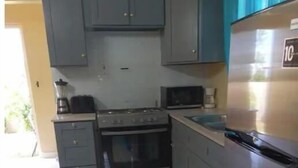 Een keuken met grijze kastjes, een fornuis, een magnetron en een koelkast.
