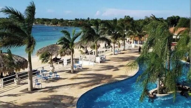 Een resort met een zwembad, palmbomen en een strand.