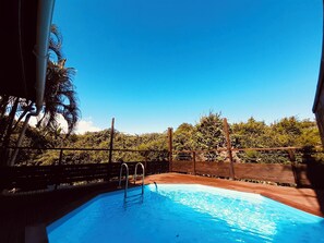 A swimming pool with metal ladders, surrounded by a wooden fence and lush greenery.