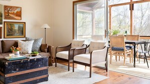 Een gezellige woonkamer met een bank, fauteuils, een tafel en een groot raam met uitzicht op bomen.