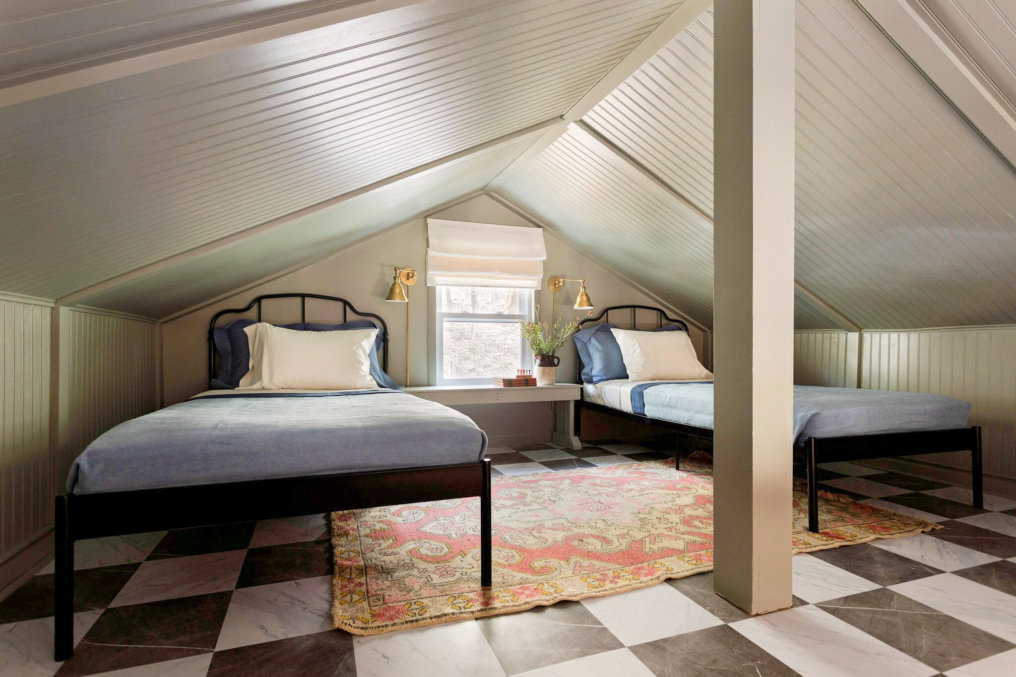 A bedroom with two beds, a window with blinds, a checkered floor, and a small table with a plant.