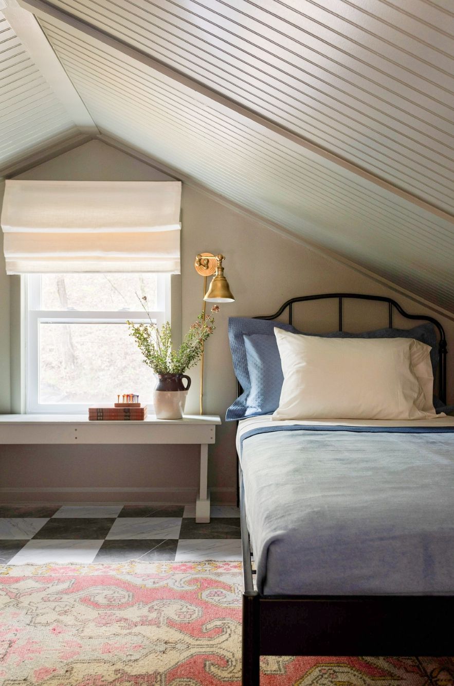 A bedroom with a bed, a window with a view, a lamp, and a plant on the windowsill.