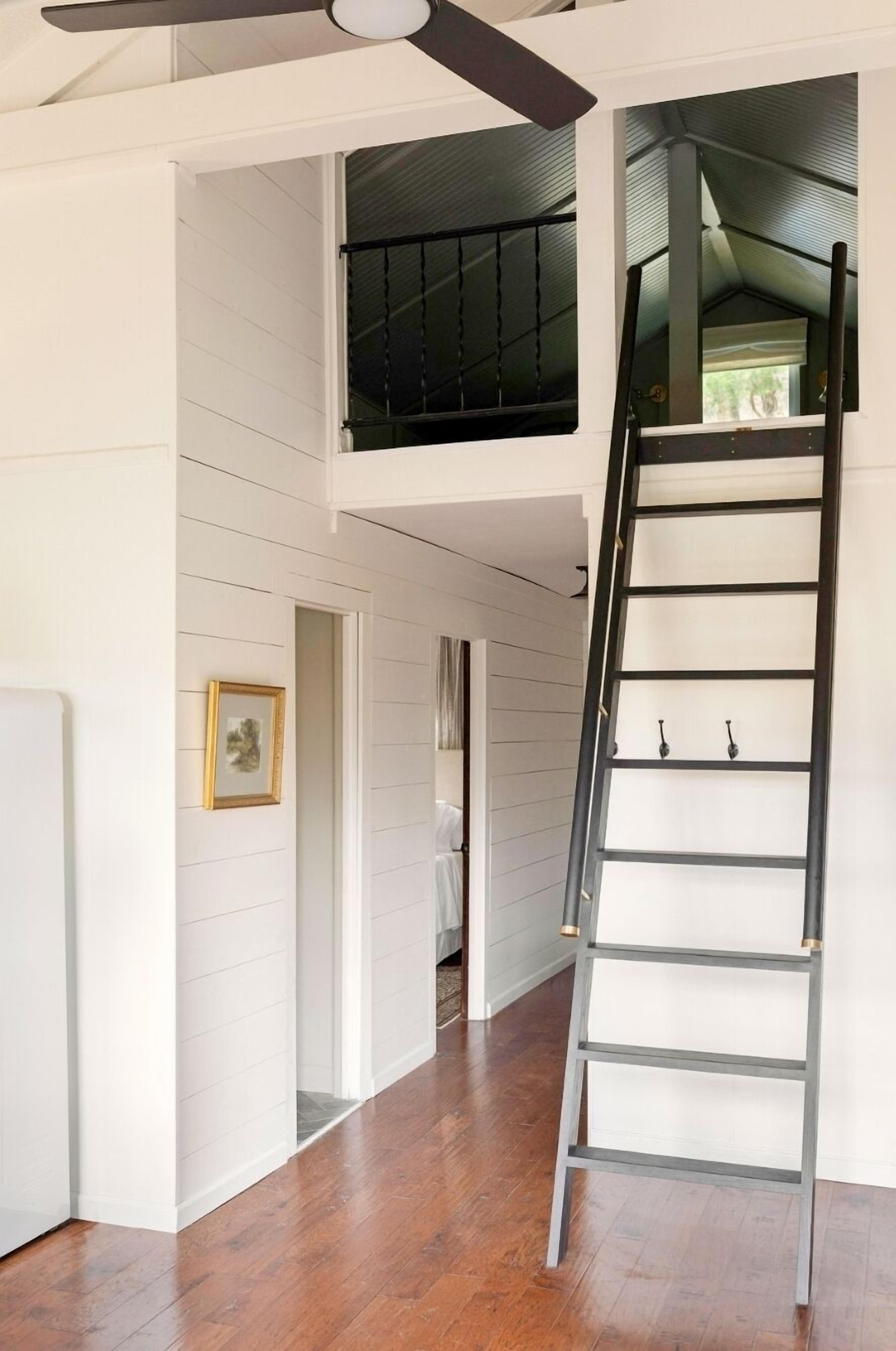 A multi-level interior with a wooden floor, a black ladder, and a ceiling fan.