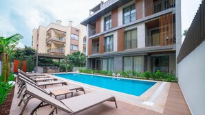 A modern hotel with a swimming pool, sun loungers, and a covered seating area. - Bomo Suites (Konyaalti)