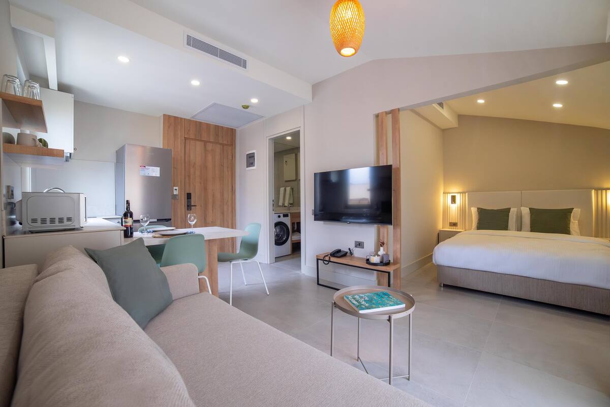Una habitación de hotel moderna con sofá, televisión, zona de comedor y dormitorio.