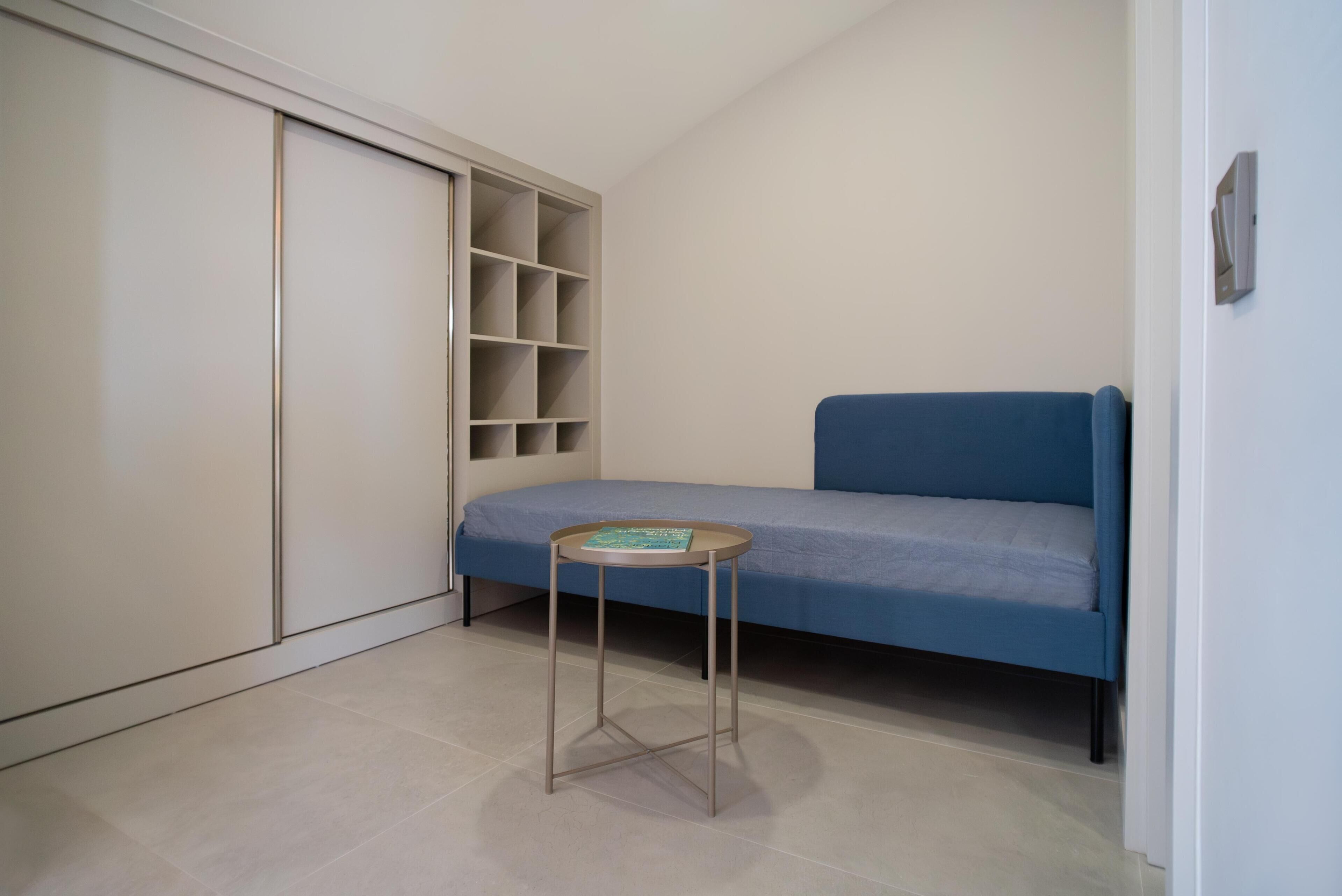 A small room with a blue sofa, a small round table with a book, and a white wardrobe with shelves.