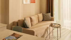 A modern living room with a beige sofa, a small round table with a cup and a book, and a hanging lamp. - Bomo Suites (Konyaalti)