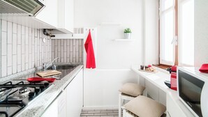 A compact kitchen with a gas stove, a sink, and a microwave. There is a red towel hanging on the wall, a small plant on a shelf, and a window providing natural light. - La Finestra sul Lago (Cernobbio)